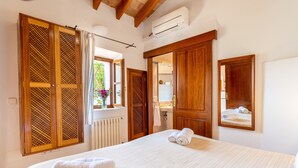 Una habitación de hotel con cama, ventana con cortinas, armario de madera, espejo y radiador.