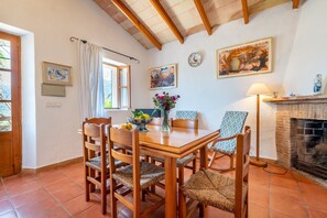 Un coin repas avec une table en bois, des chaises, un vase de fleurs, une horloge et une cheminée.