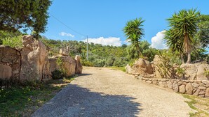 A gravel path leading through a rustic stone wall, surrounded by greenery and palm trees. - Holiday Home "Casa Relax Vista Mozzafiato" with Garden & A/C (Cannigione)