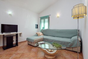 Ett vardagsrum med en tv på ett tv-bord, en soffa, ett soffbord i glas och en golvlampa.