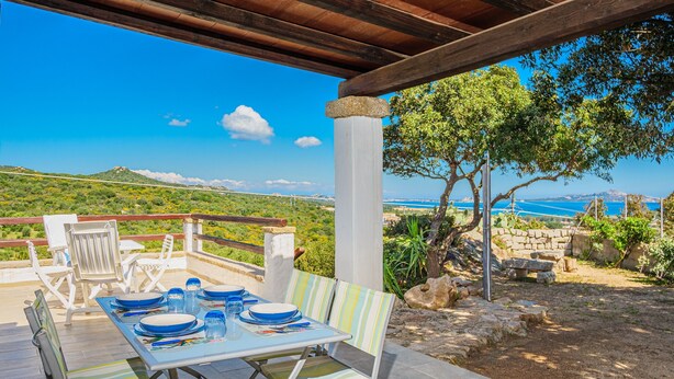 An outdoor dining area with a table set for two, overlooking a scenic landscape with hills and a body of water. - Holiday Home "Casa Relax Vista Mozzafiato" with Garden & A/C (Cannigione)