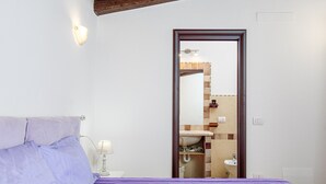 A bedroom with a bed, a nightstand with a lamp, a mirror, and a bathroom visible through an open door. - Holiday Home "Casa Relax Vista Mozzafiato" with Garden & A/C (Cannigione)