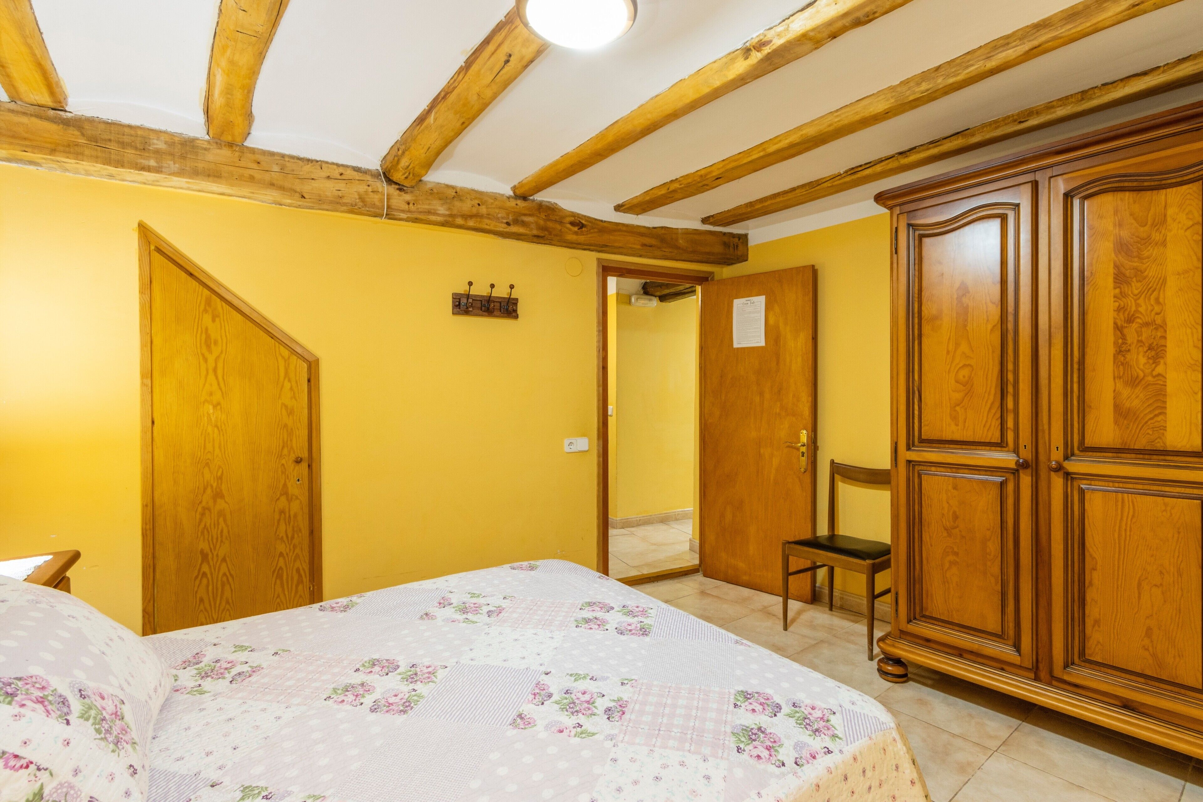 A room with a bed, wooden wardrobe, and a door leading to another room.