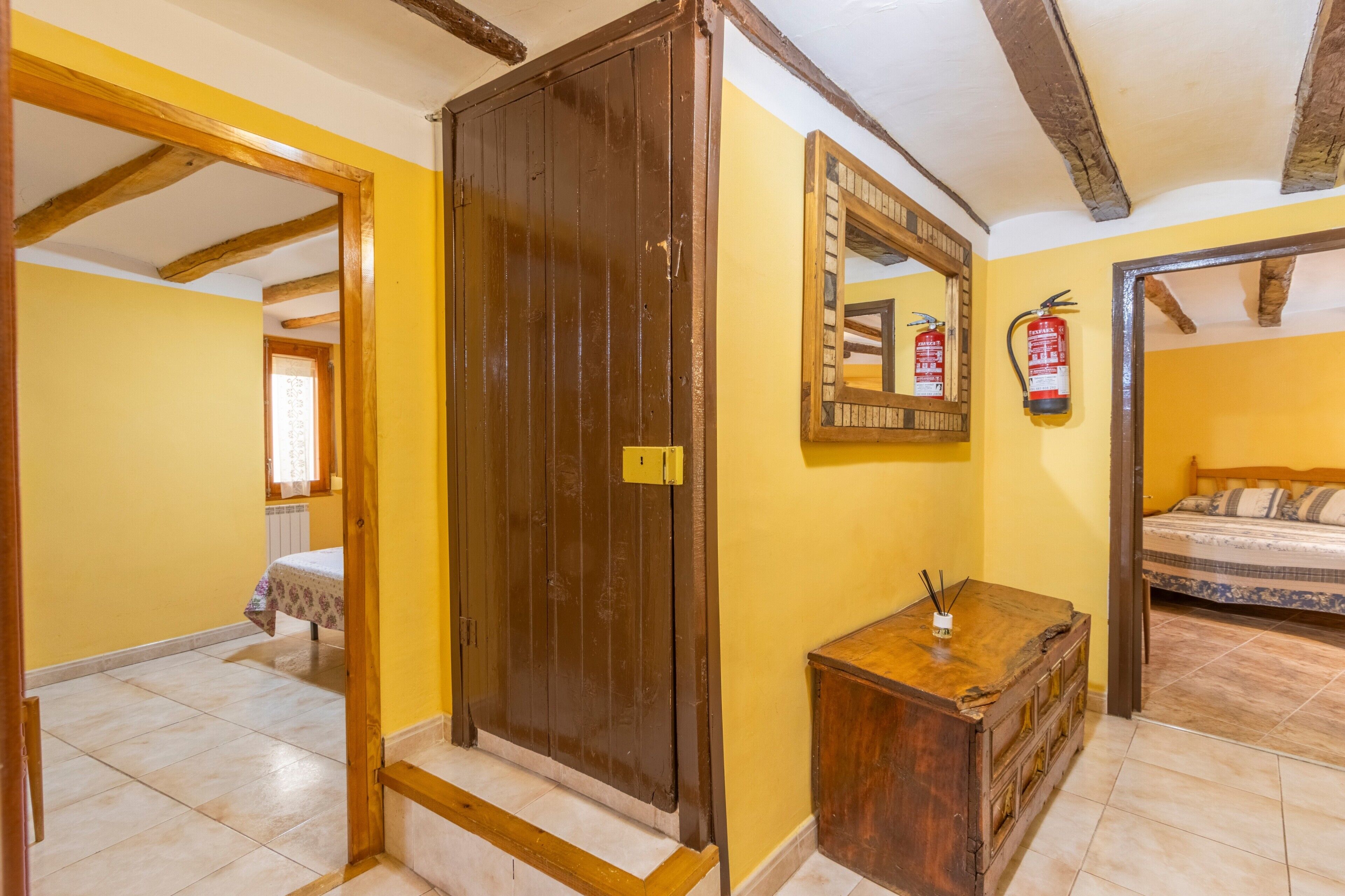 Una habitación con un armario de madera, una mesita de noche con lámpara, una cama con colcha estampada y un espejo en la pared.