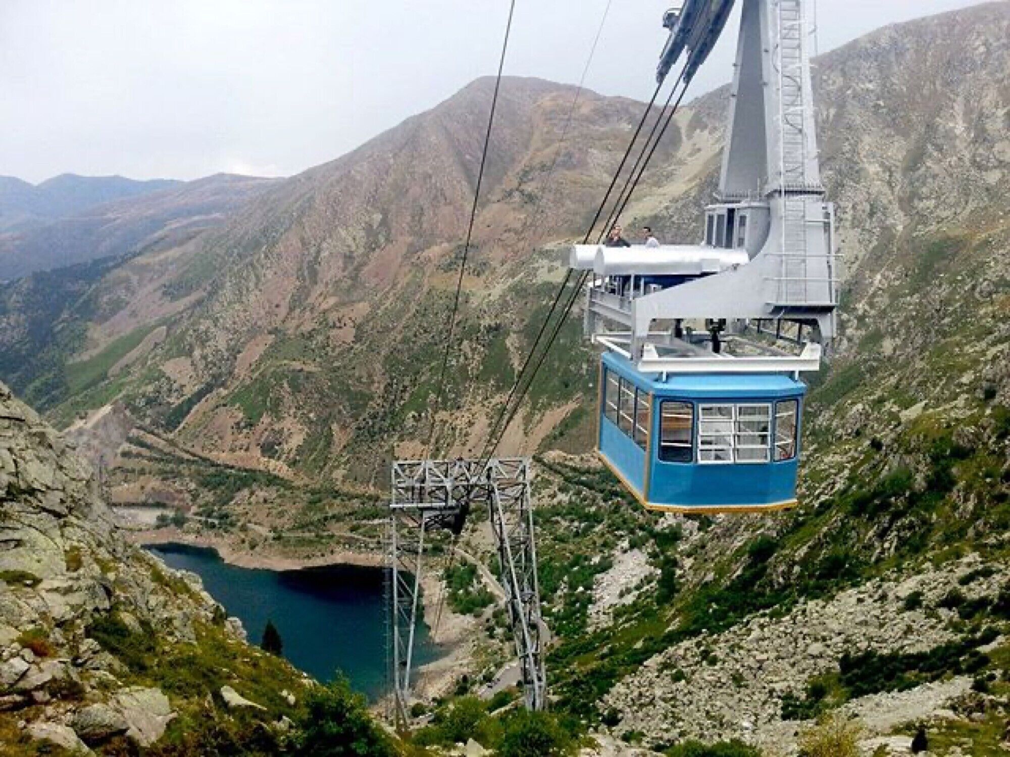 A cable car system with a blue cabin, a mountainous landscape, and a lake below.