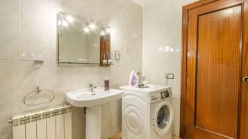 A bathroom with a sink, mirror, radiator, washing machine, and wooden door.