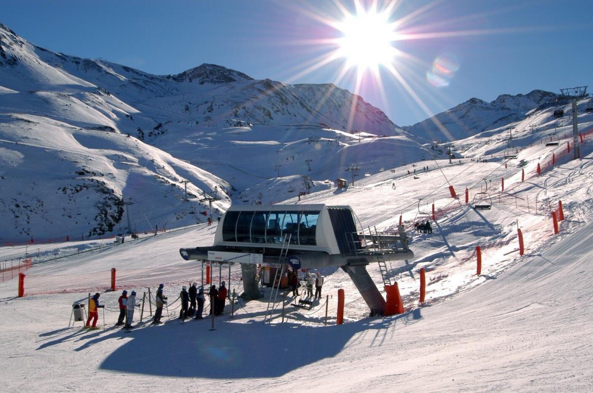 Estación de telesilla con un ascensor de sillones, pistas nevadas y cielo despejado.