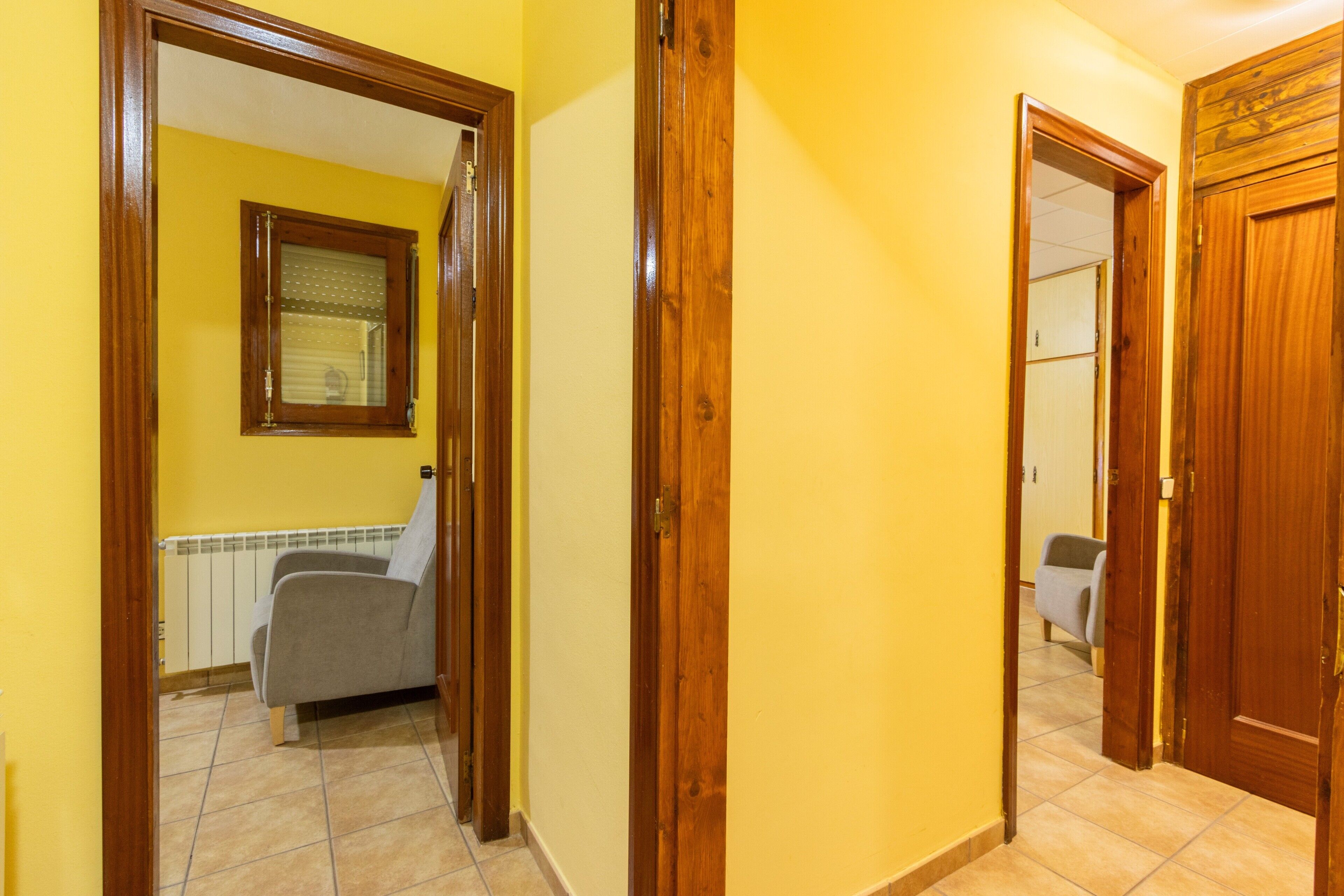 Un couloir avec des portes en bois, un radiateur et une chaise.