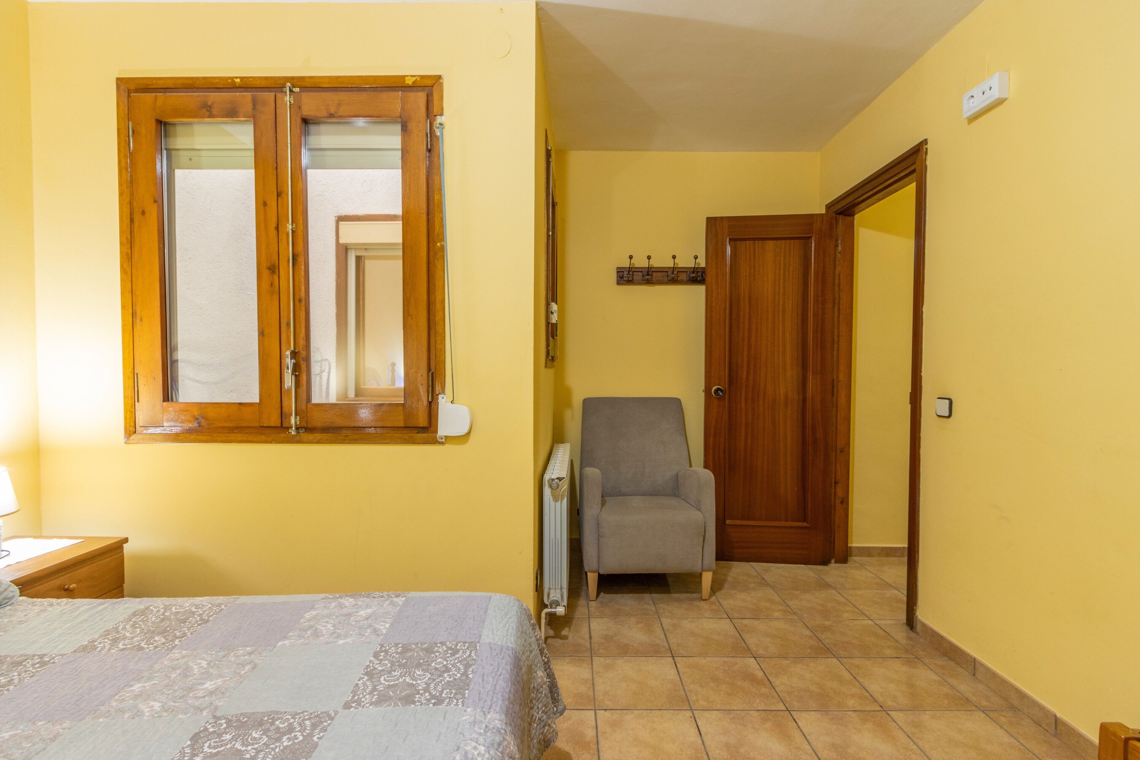 Un dormitorio con cama, una silla, una puerta de madera y un radiador.