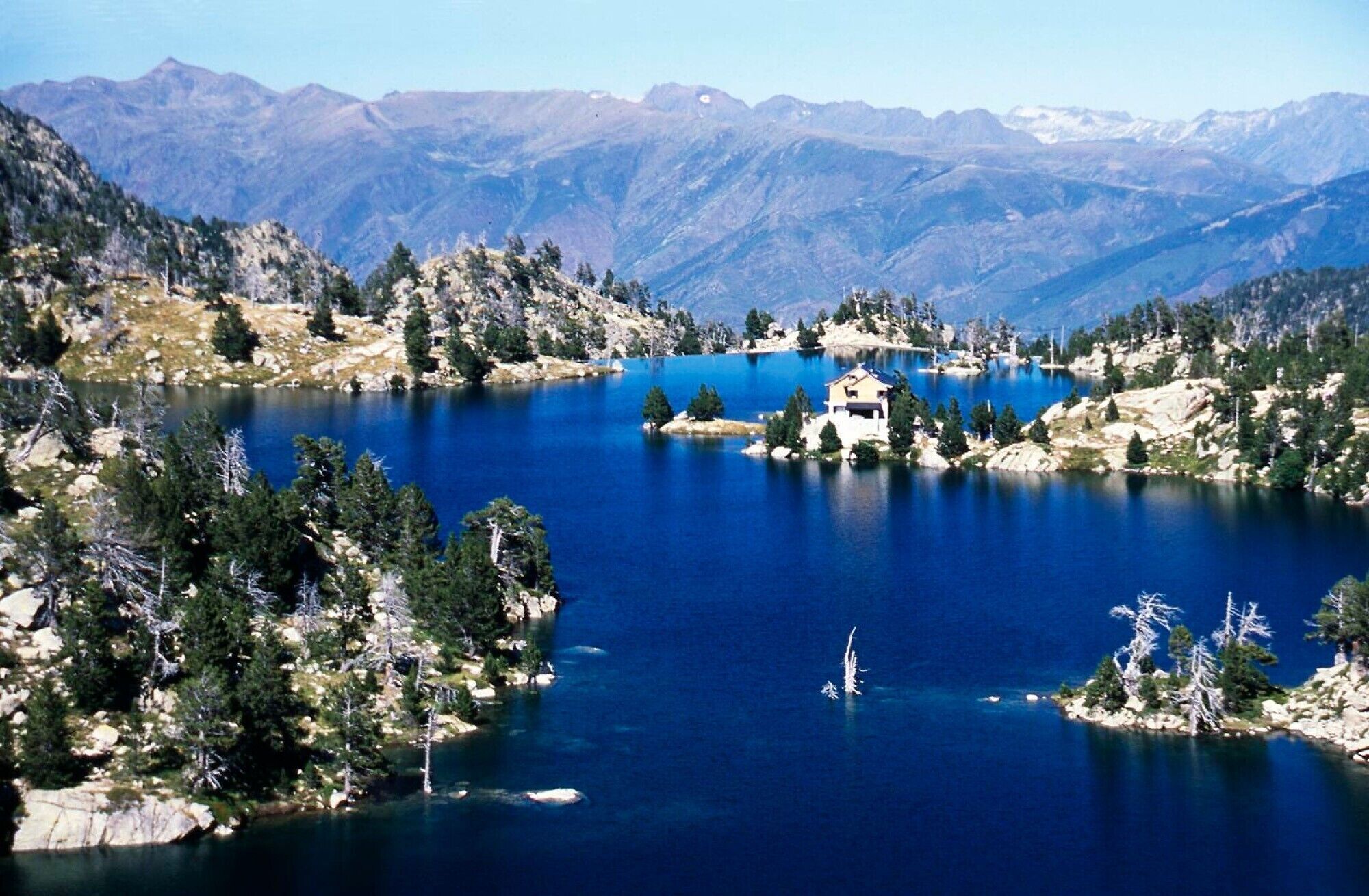 Un lago rodeado de montañas, una pequeña casa en una isla y densas áreas boscosas.
