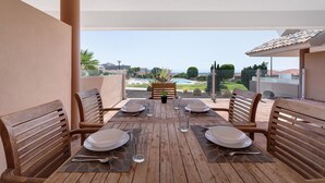Mesa de madera preparada para cuatro personas, con sillas, vista a una piscina y un paisaje urbano al fondo.