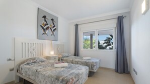 Un dormitorio con dos camas, un radiador, una ventana con cortinas y un cuadro en la pared.