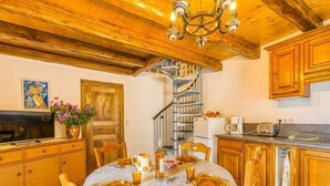 A cozy kitchen with wooden cabinets, a dining table set for four, and a spiral staircase leading to an upper level.