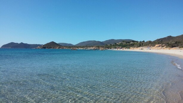 Una platja amb aigua cristal·lina, sorra daurada i muntanyes al fons.