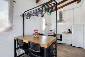 A kitchen with a wooden table, black chairs, a hanging pot rack, and white cabinets. - Vacation Home 'Ca Lajares' with Mountain View, Private Terrace and Wi-Fi (Lajares)