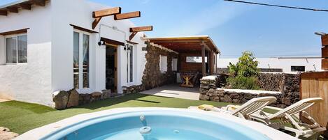A swimming pool with lounge chairs, a stone wall, and a white building with wooden beams.
