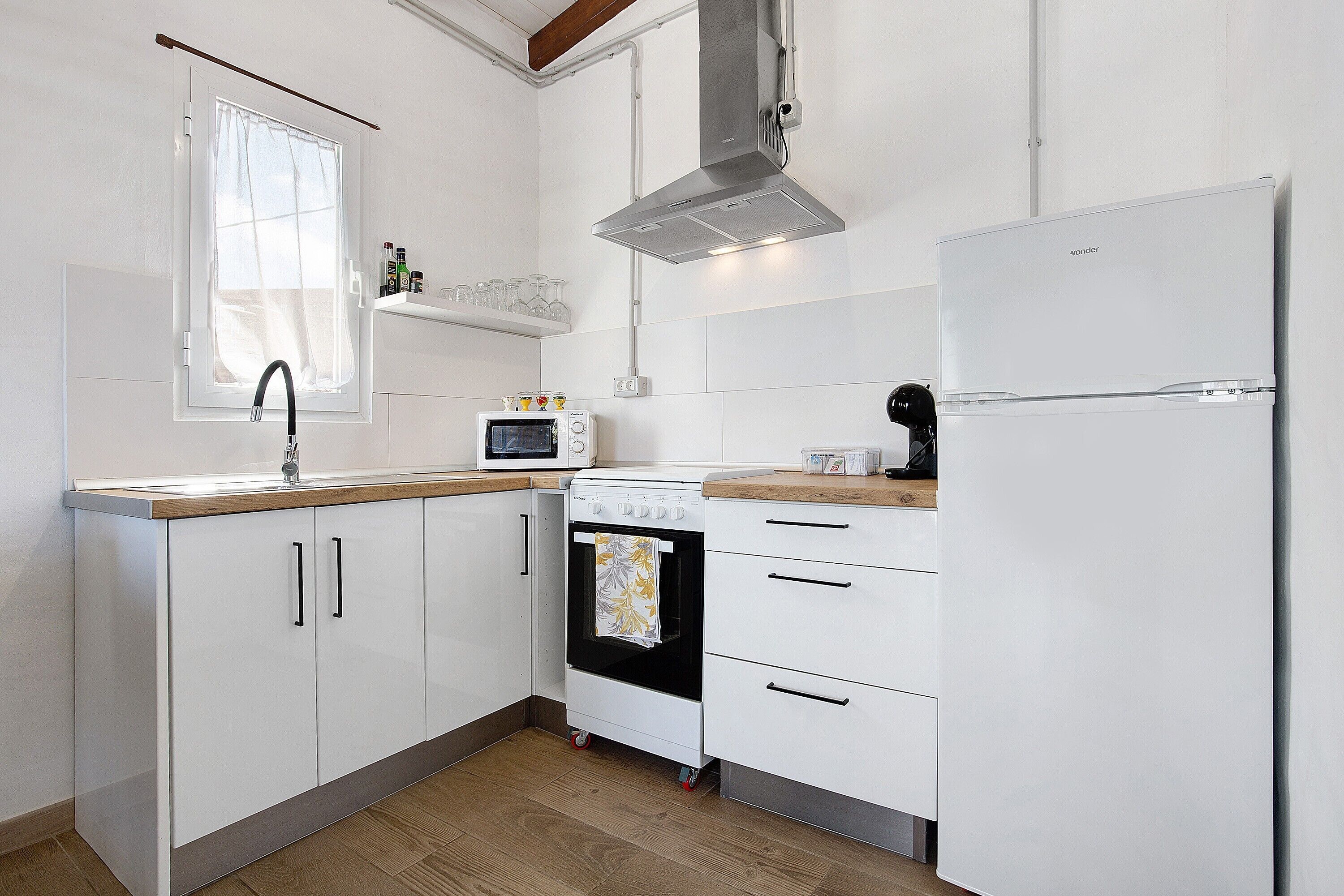 A kitchen with white cabinets, a microwave, an oven, a stainless steel range hood, and a refrigerator.