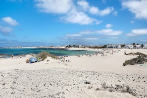 A beach with people, a clear sky, and buildings in the background. - Vacation Home 'Ca Lajares' with Mountain View, Private Terrace and Wi-Fi (Lajares)
