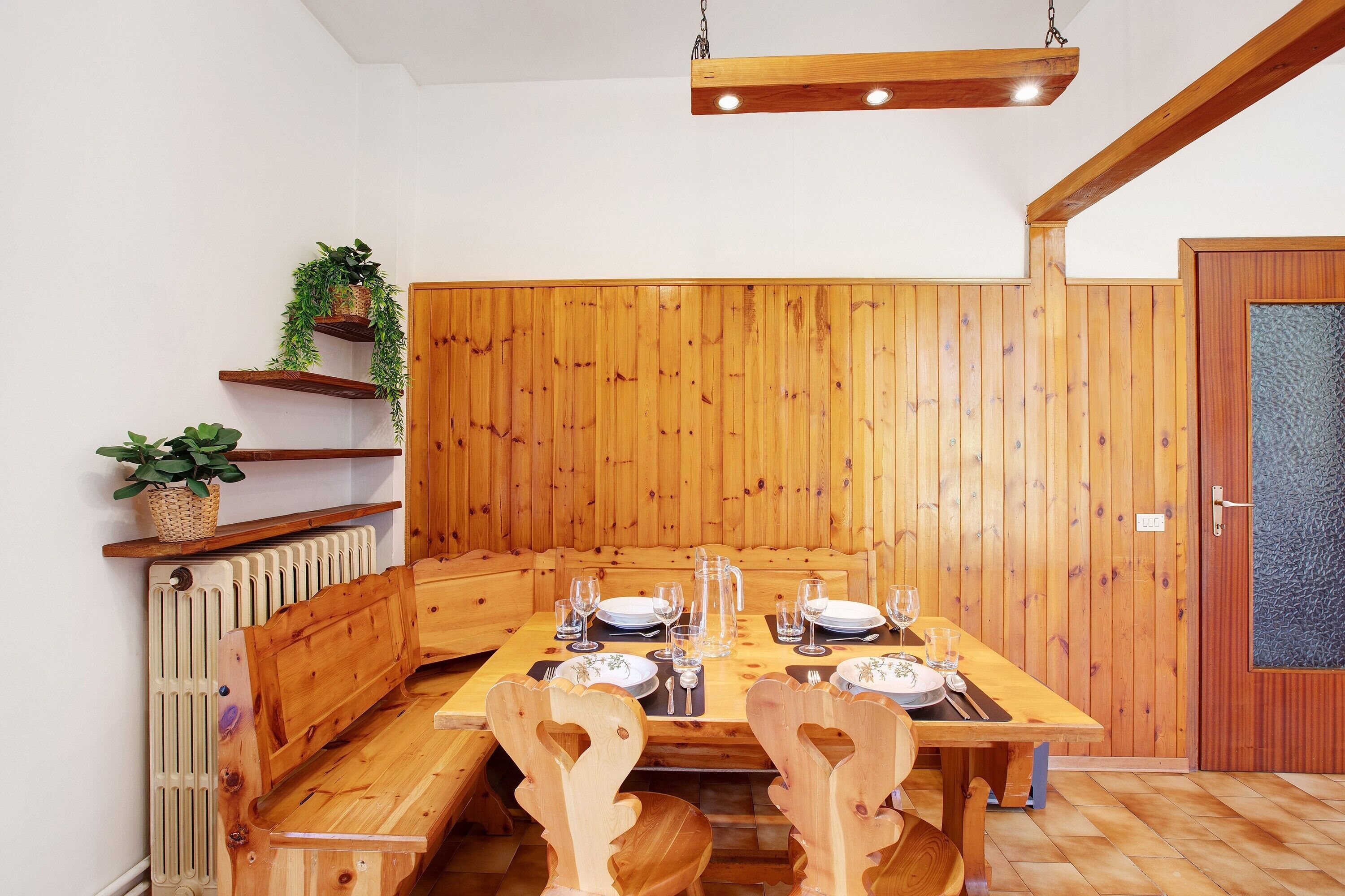 Une table de salle à manger en bois, mise avec des assiettes, des verres et un pichet, entourée de chaises en bois.