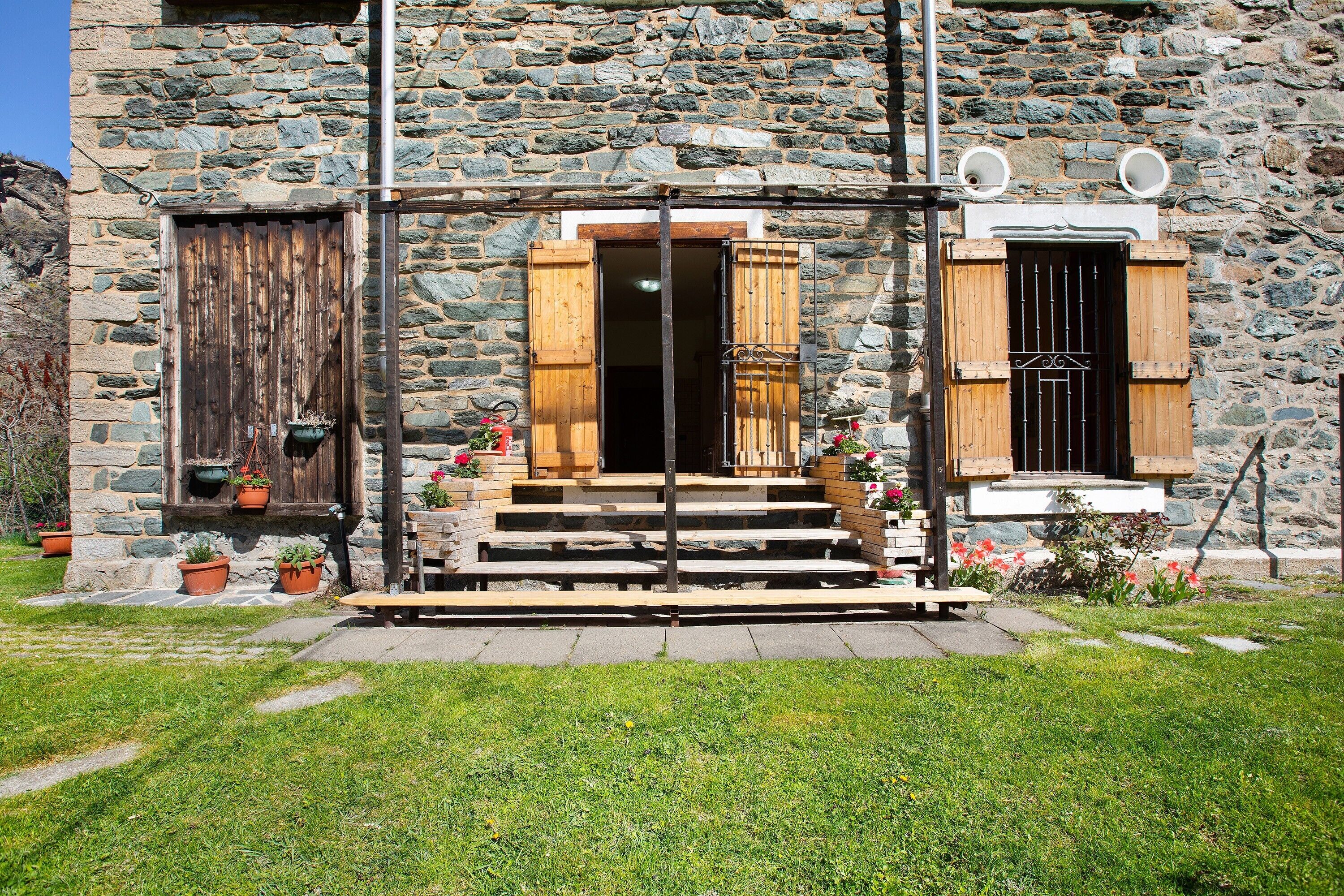 A stone building with a wooden door, a window with shutters, and a small porch with steps.