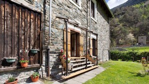 A stone building with a wooden porch, steps, and potted plants. - Apartment 'Casa Tua - Avise' with Mountain View, Private Terrace and Wi-Fi (Runaz)