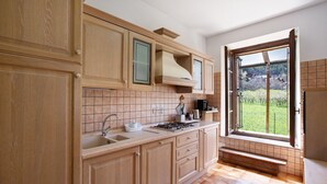 A kitchen with wooden cabinets, a sink, a stove, and a window with a view of greenery. - Apartment 'Casa Tua - Avise' with Mountain View, Private Terrace and Wi-Fi (Runaz)