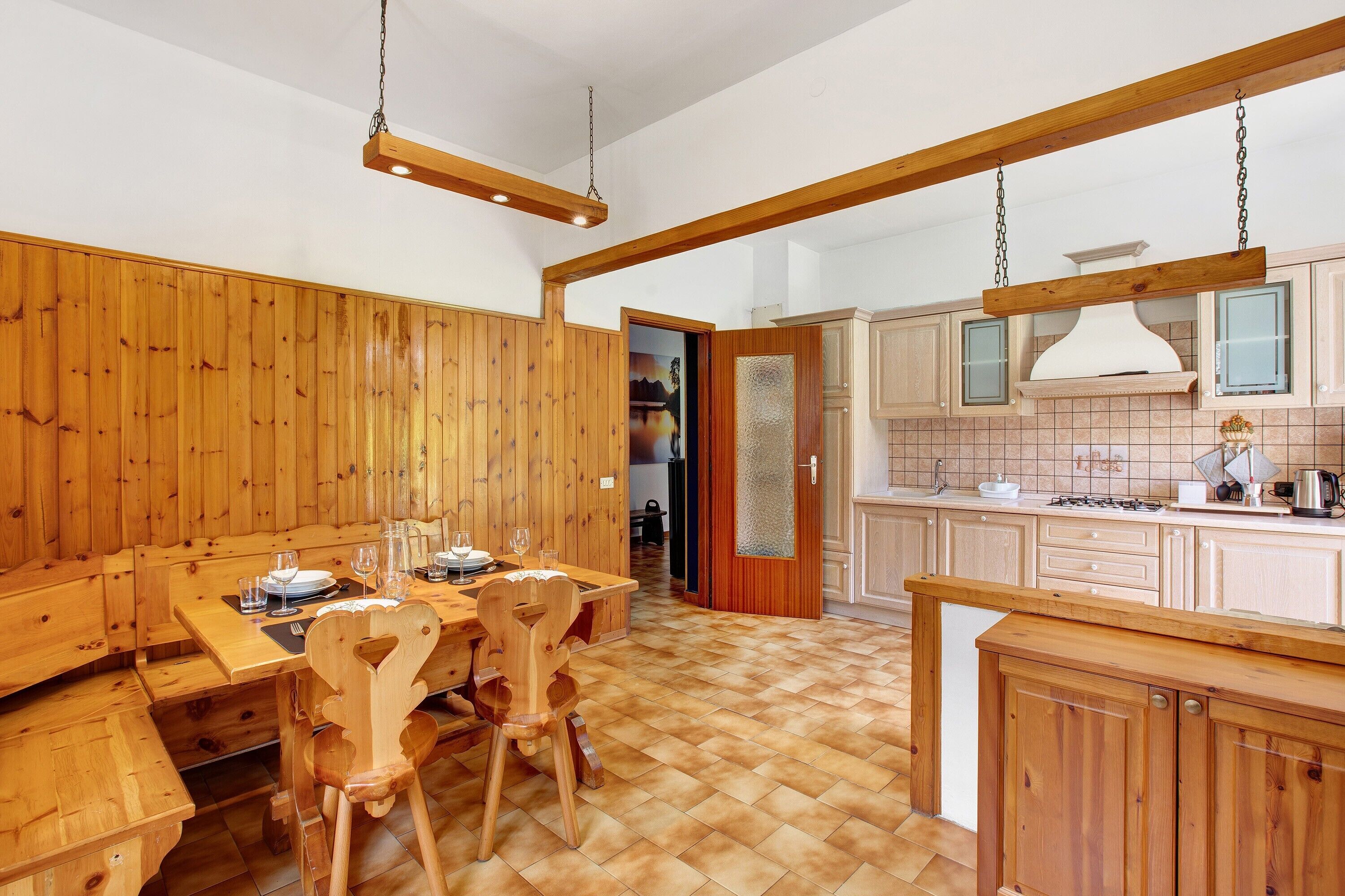 A wooden dining area with a bench and chairs, a kitchen with wooden cabinets, and a hanging light fixture.