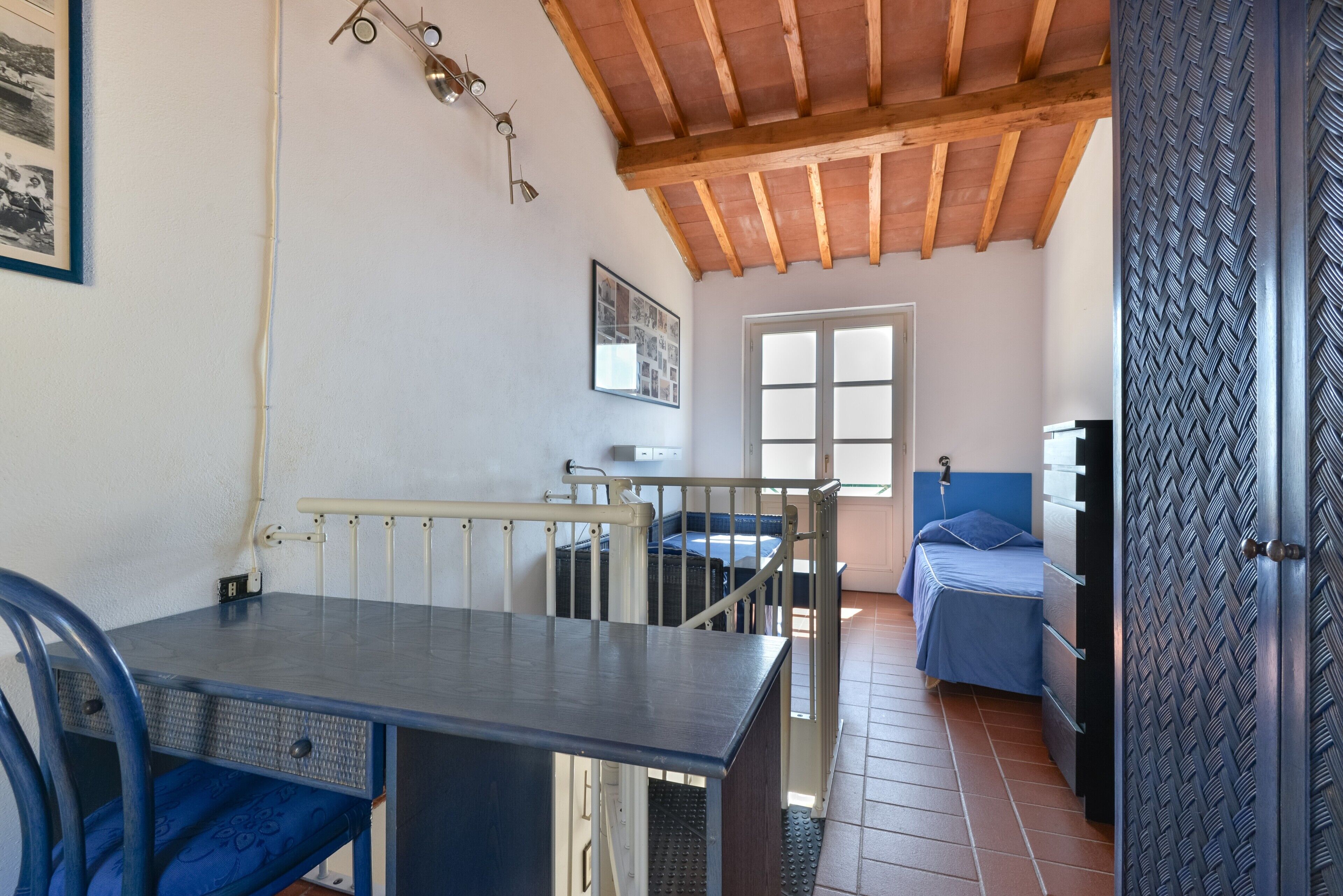 A room with a bed, a table, a chair, a window, and a door with a patterned design.