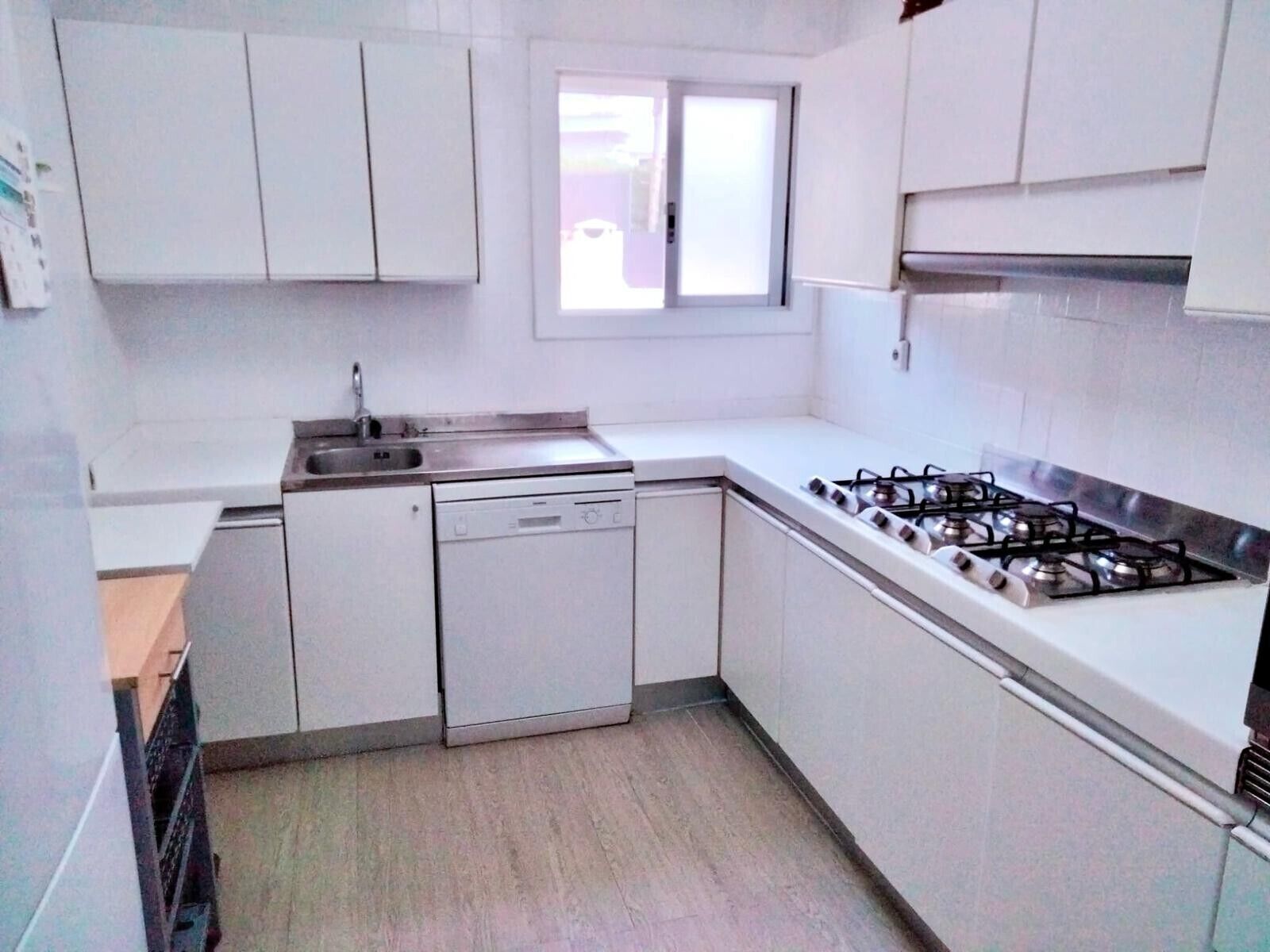 A compact kitchen with white cabinets, a gas stove, a dishwasher, and a window.