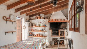 Ein rustikaler Raum mit einem Bett, Regalen mit Keramik, einem Kamin und einer Holzzieldecke.