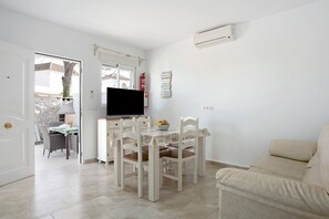 Un salon avec un canapé beige, une table à manger avec des chaises, un téléviseur à écran plat et un extincteur fixé au mur.