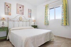 Une chambre à coucher comprenant un lit, deux tables de chevet, une fenêtre avec des rideaux et des œuvres d’art murales.