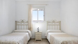 A twin bedroom with two beds, a nightstand, a window with curtains, and a tiled floor.