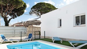 A swimming pool with lounge chairs, a white building, and a tree.