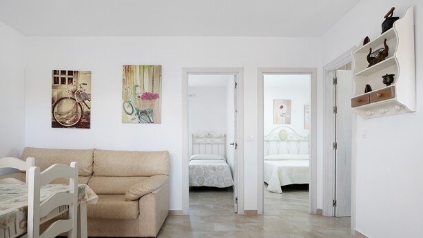 A room with a bed, a chair, a table, and a door leading to another room.