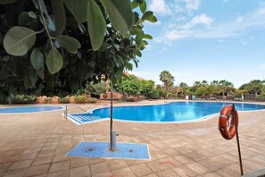 A swimming pool with a lifebuoy, surrounded by greenery and a clear sky. - Vacation Home "Ático Beach Sotavento" with Shared Pool & Wi-Fi (Granadilla)