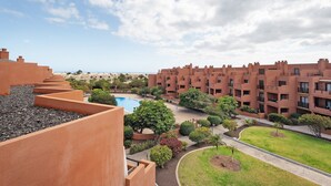A residential building with a swimming pool, green lawns, and a clear sky.