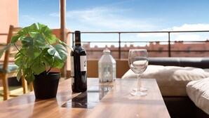A balcony with a potted plant, a bottle of wine, and a wine glass on a wooden table.