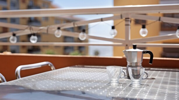 En balkong med ett metallbord, två glas och en kaffekanna.