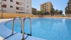 En swimmingpool med metallräcken, omgiven av byggnader med balkonger och palmer.