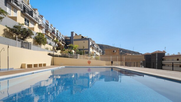A swimming pool with a clear blue water surface, surrounded by a low-rise building with balconies and a small hill in the background. - Vacation Home "Vivienda Vacacional Atlántida" with 2 Shared Pools, 2 Private Terraces & Wi-Fi (Caletillas)