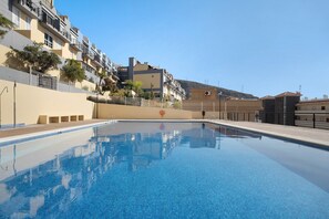 Une piscine à l’eau d’un bleu limpide, entourée d’un bâtiment de faible hauteur doté de balcons, avec une petite colline en arrière-plan.