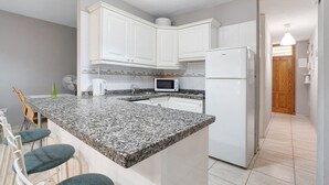 A kitchen with white cabinets, a granite countertop, a microwave, a refrigerator, and a dining area with chairs. - Vacation Home "Vivienda Vacacional Atlántida" with 2 Shared Pools, 2 Private Terraces & Wi-Fi (Caletillas)