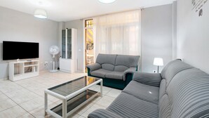 A modern living room with a flat-screen TV, a glass coffee table, a sofa, a fan, and a lamp. - Vacation Home "Vivienda Vacacional Atlántida" with 2 Shared Pools, 2 Private Terraces & Wi-Fi (Caletillas)