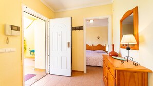 Habitación de hotel con una cama, un tocador de madera, un espejo y una puerta que da a otra habitación.