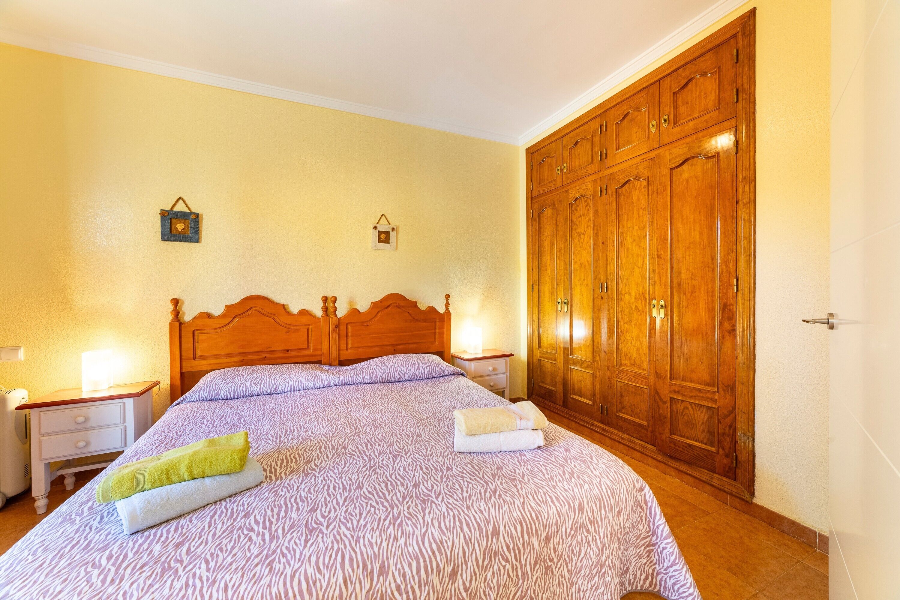 A bedroom with a bed, wooden wardrobe, bedside tables, and wall-mounted lamps.