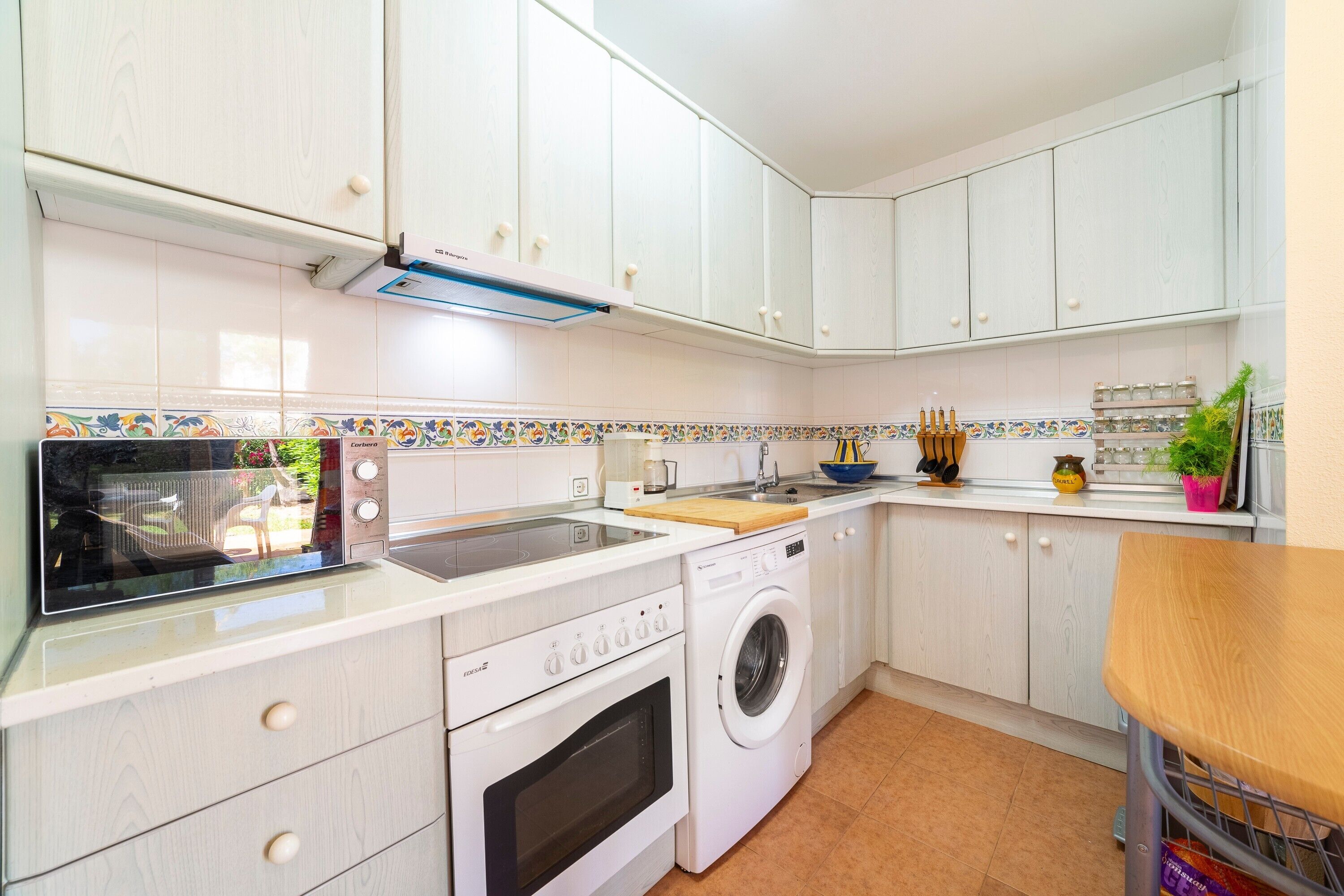 A kitchen with white cabinets, a microwave, a washing machine, and a wooden countertop.
