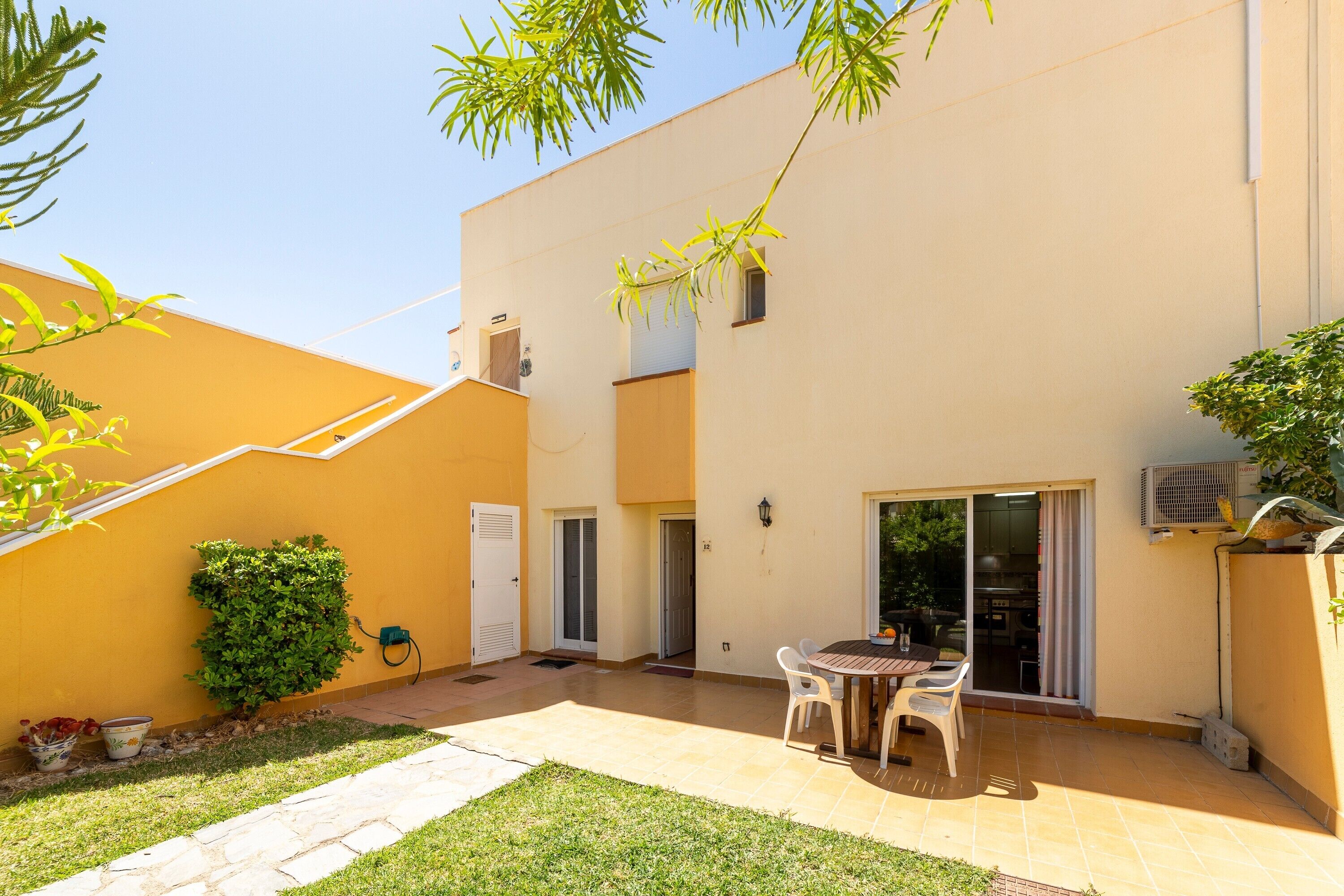 A patio with a table and chairs, a small garden, and a building with a yellow exterior.