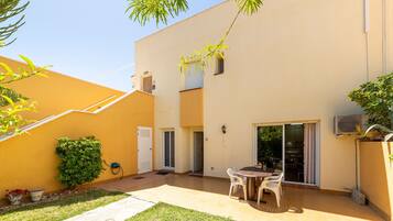 A patio with a table and chairs, a small garden, and a building with a yellow exterior.
