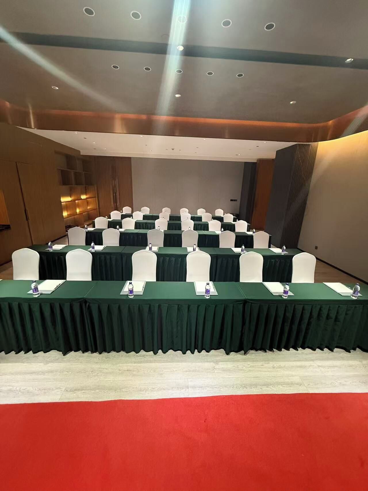 Un salón de conferencias con filas de mesas, sillas y una alfombra roja.
